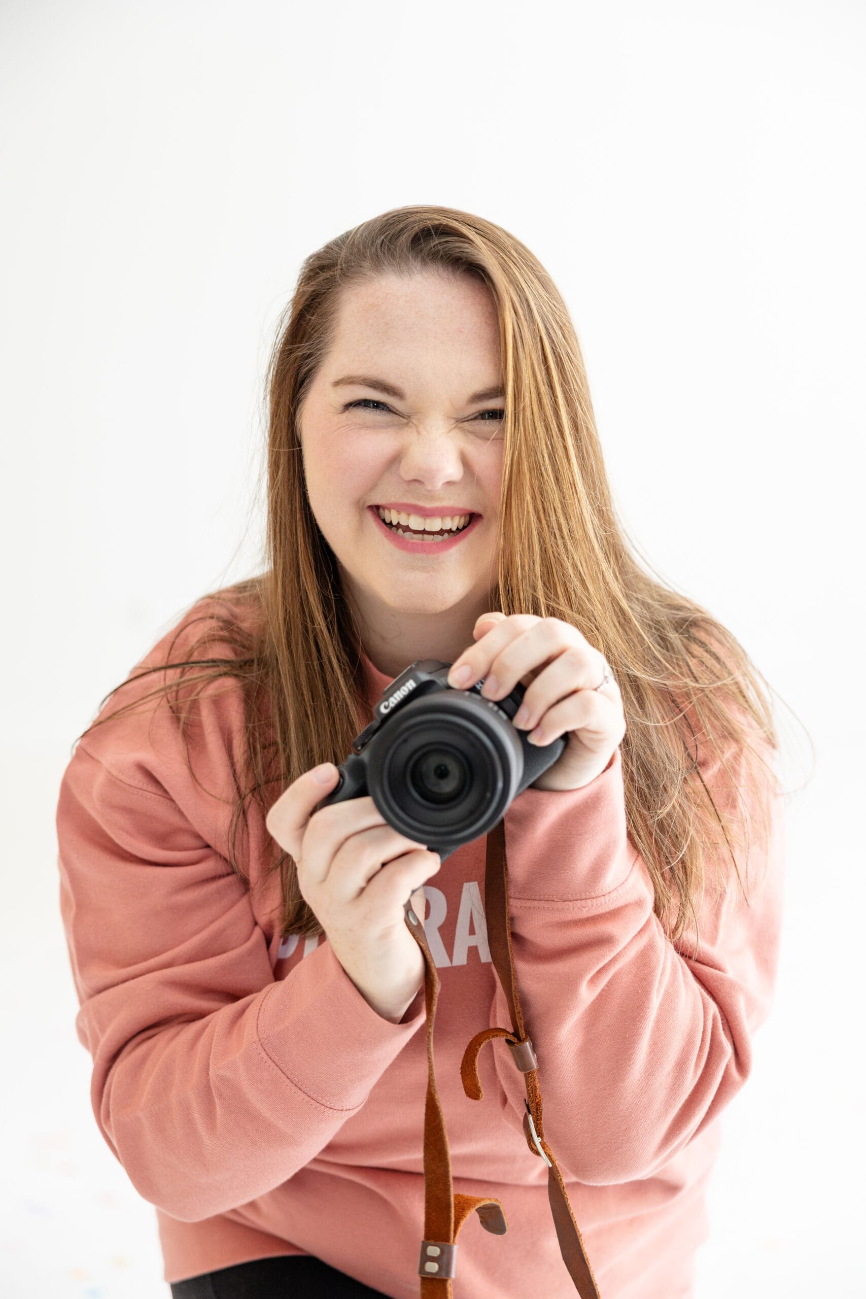 Woman in salmon colored sweater holds up camera and laughs | Make Marketing Easier | Kayla Petrosky Photography