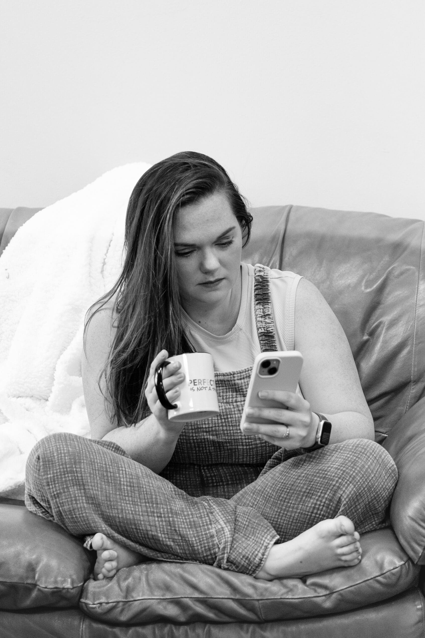 Black and white image of woman on a couch looking at phone and drinking coffee | Make Marketing Easier | Kayla Petrosky Photography