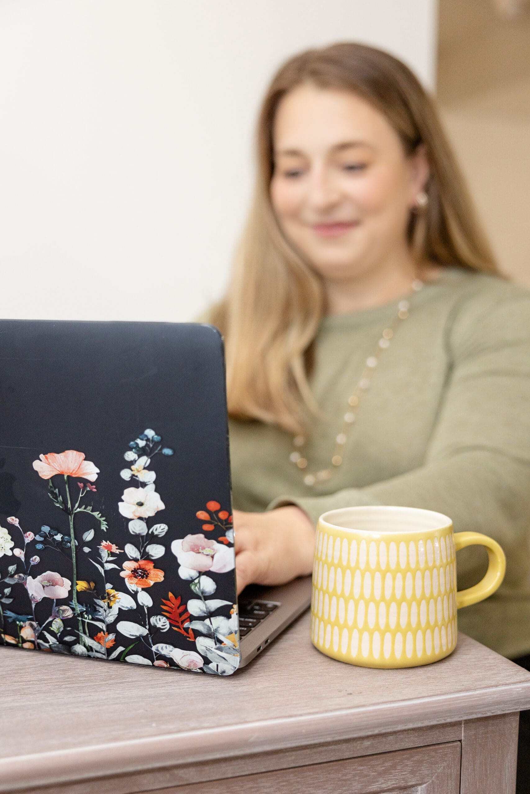 Woman sits at desk with floral decorated laptop and yellow coffee mug | How to choose your brand photographer | Kayla Petrosky Photography
