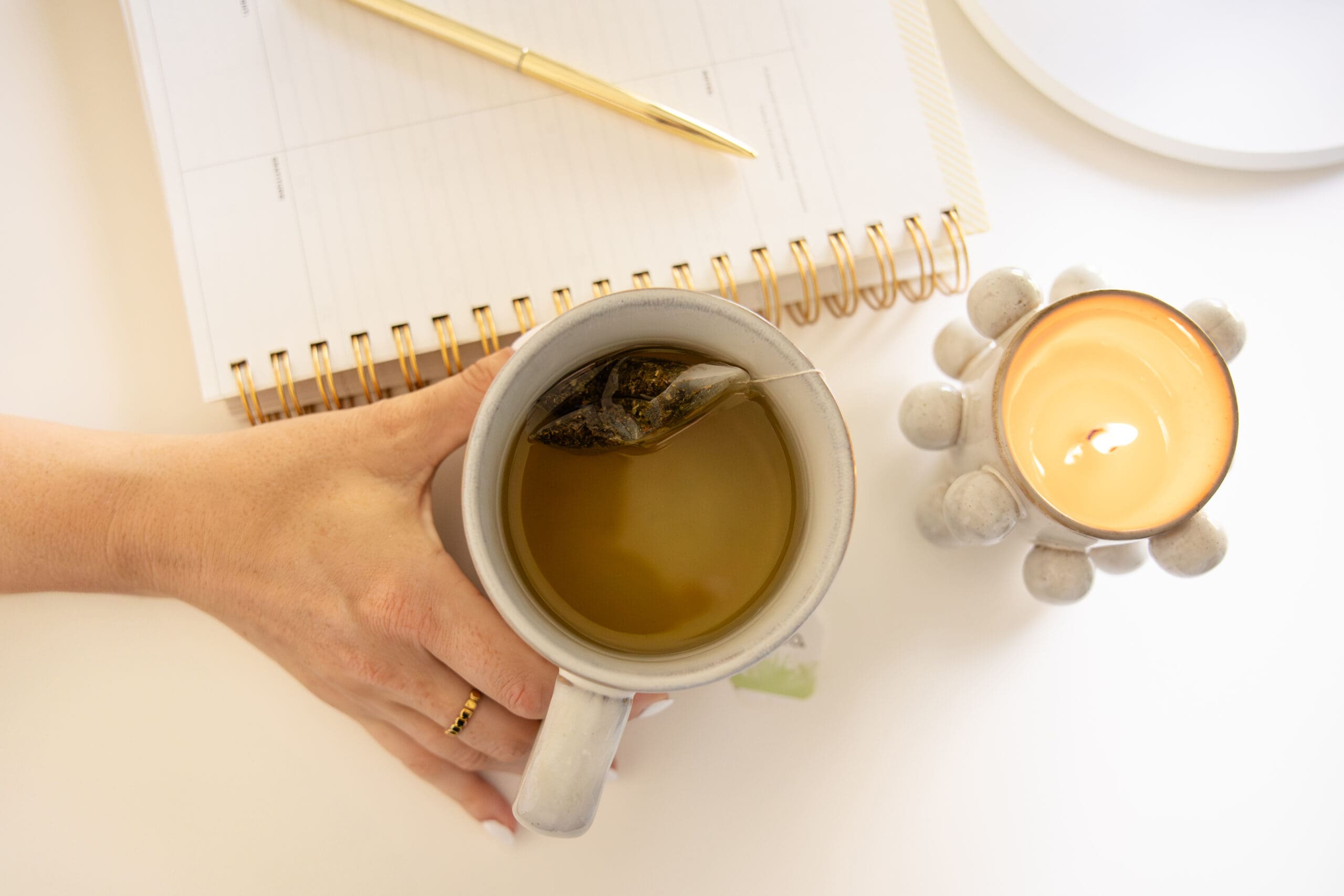 Hand reaches for mug of tea nestled between lit candle and planner | Mindset Coach Brand Photos | Kayla Petrosky Photography
