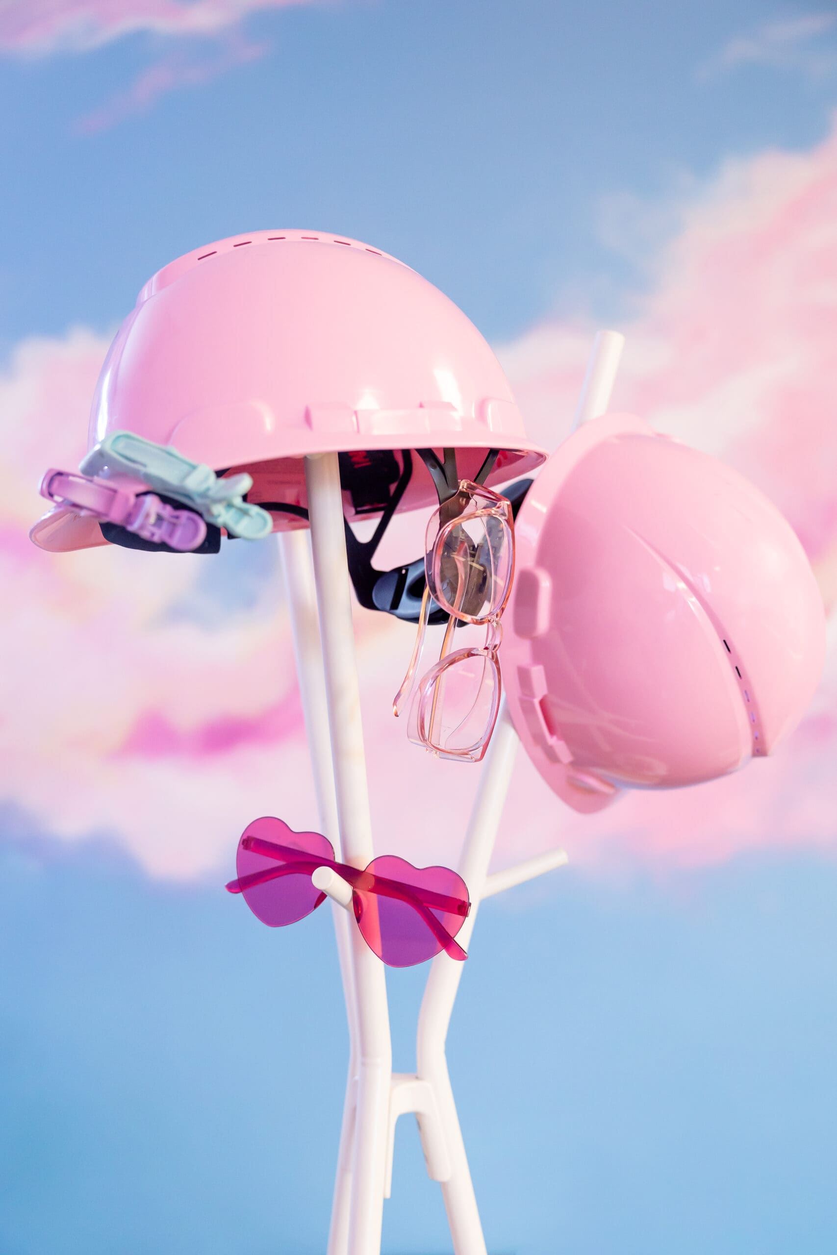 Pink hard hats and sunglasses hang on a white coat rack | hair studio brand photos