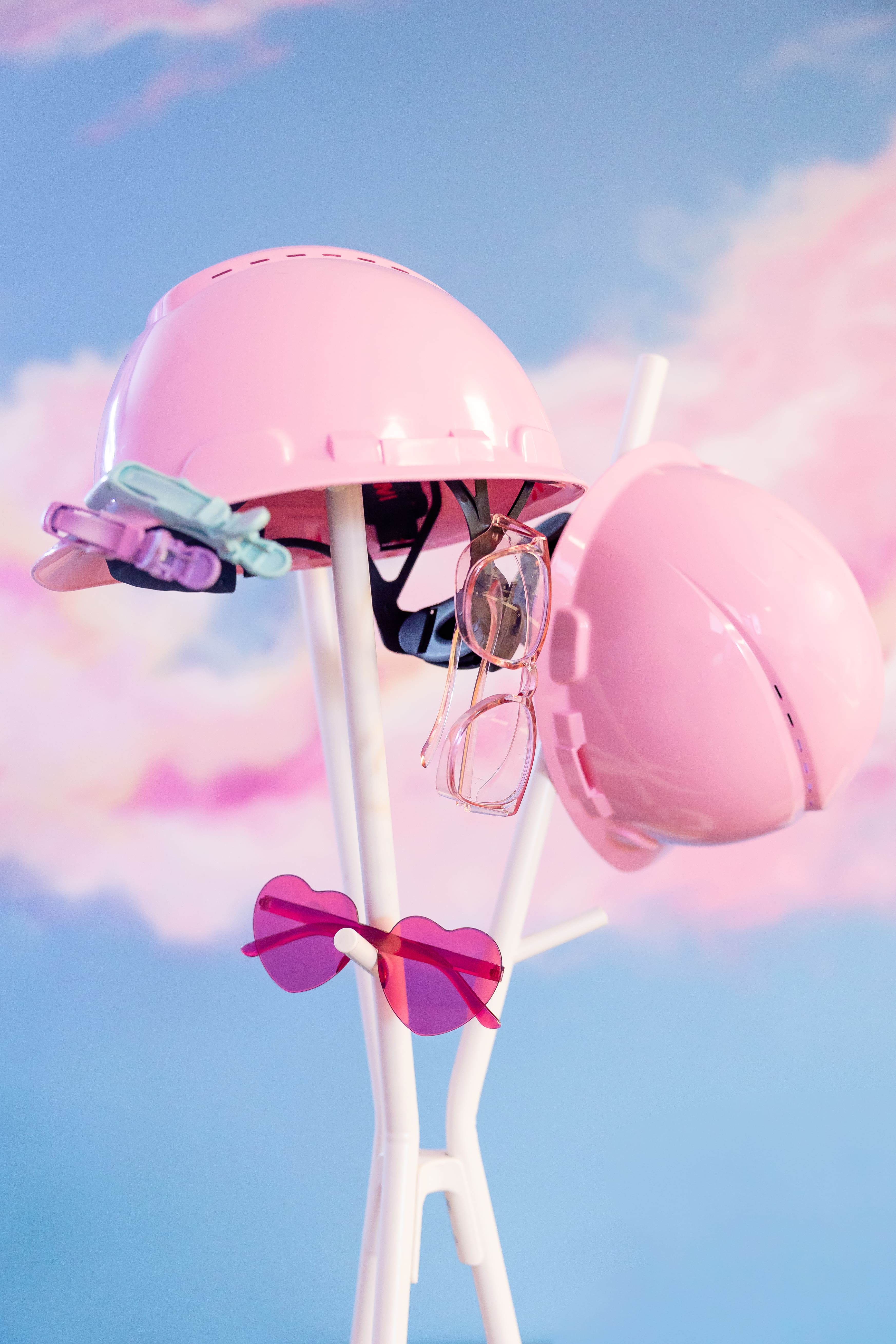 Pink hard hats and sunglasses hang on a white coat rack | hair studio brand photos