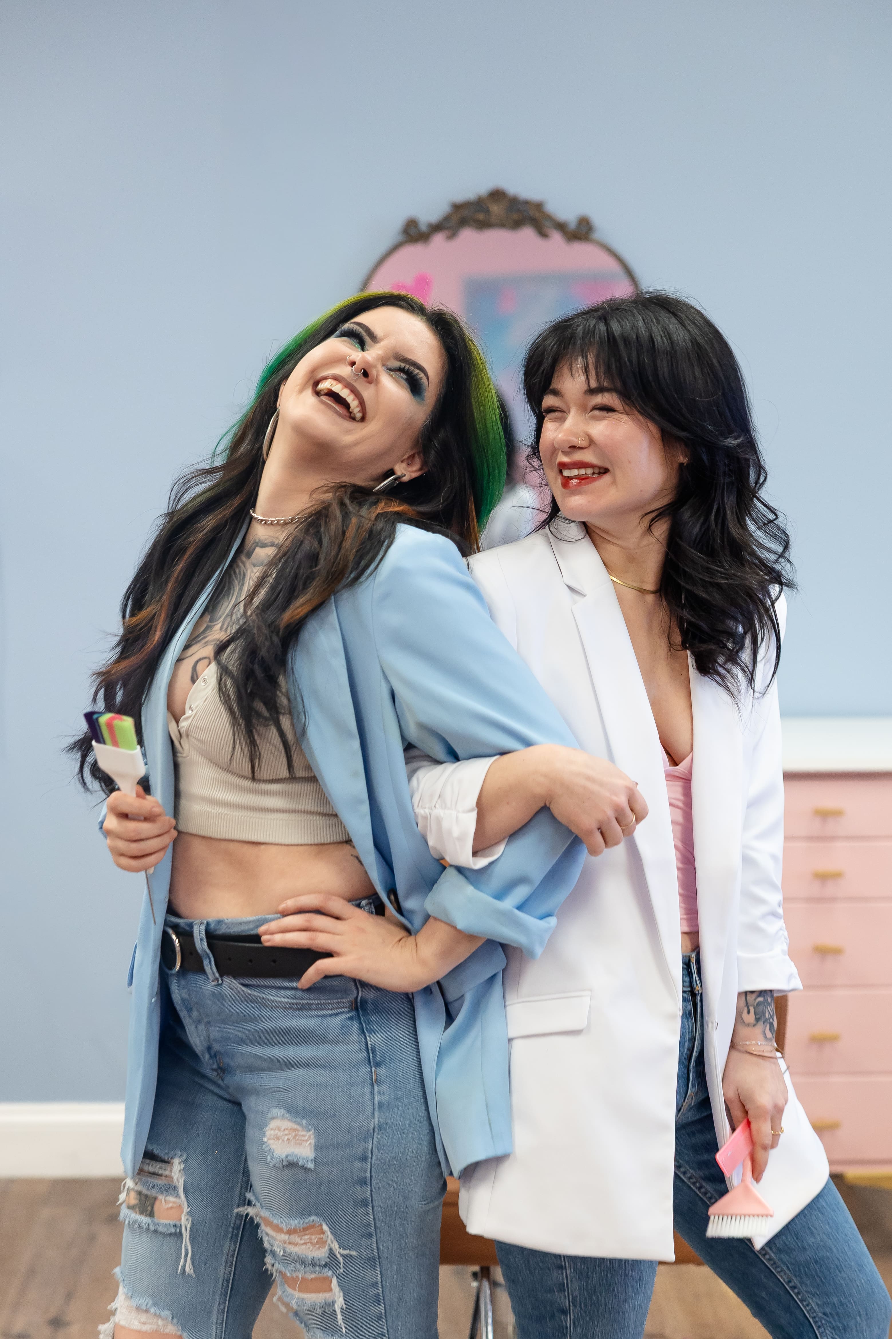 Two white women link arms and look at each other while laughing | Hair studio brand photos